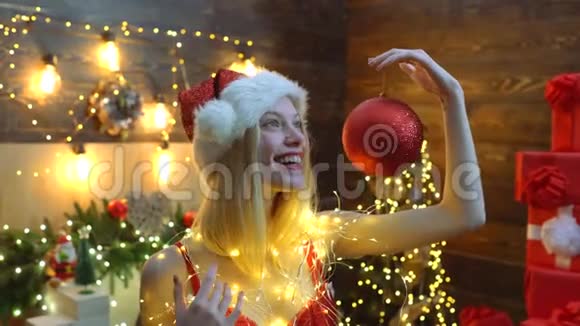圣诞派对性感的金发女人拿着红色的圣诞球在圣诞树后面圣诞装饰品新视频的预览图