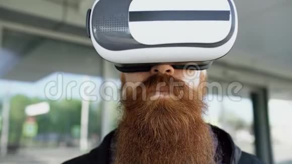 使用虚拟现实耳机进行360VR体验并带着微笑在户外的眼镜为年轻大胡子男士提供特写视频的预览图