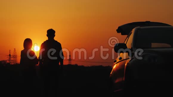 一对年轻夫妇正站在他的车旁边在宾馆上空欣赏日落视频的预览图