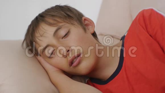 年轻人睡在沙发上白天睡在米色皮革沙发上的穿红色t恤的白种人少年特写视频的预览图