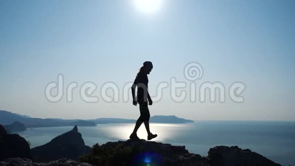 年轻的长发男子走在一个尖锐的山脊上迎着美丽的蓝色向海面的山顶走去视频的预览图