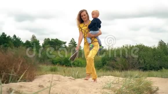 快乐的母亲和她的小男孩挽着胳膊穿过沙丘视频的预览图