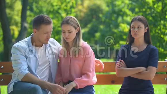 恋爱中的情侣坐在长凳上拥抱和聊天无视他们的朋友视频的预览图
