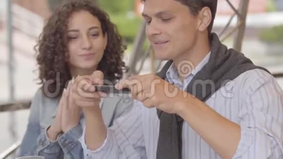 帅哥和可爱的女人在餐馆里用手机拍照他们的食物快乐的一对享受视频的预览图
