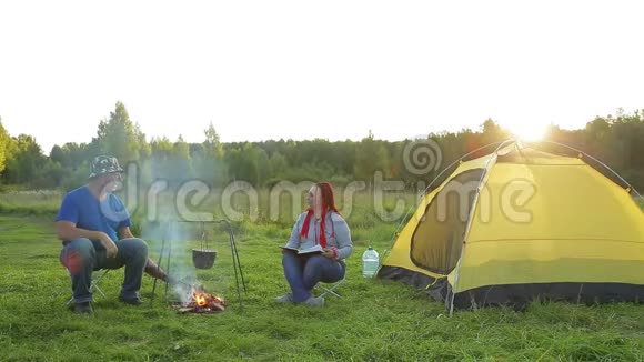 一个男人和一个女人在篝火附近的帐篷附近读一本书看沸腾的锅视频的预览图