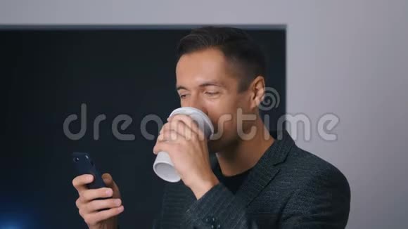 自信的商人在咖啡休息期间喝咖啡在办公室里使用智能手机视频的预览图