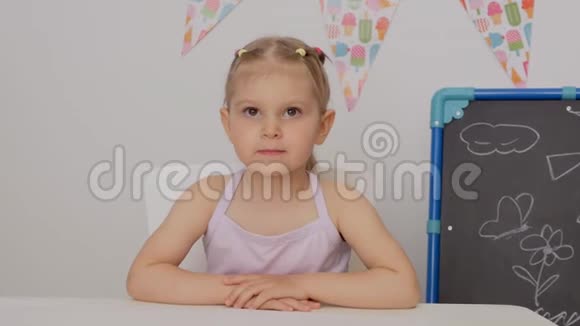 一个小女孩坐在孩子们房间桌子旁小心翼翼地看着前方视频的预览图