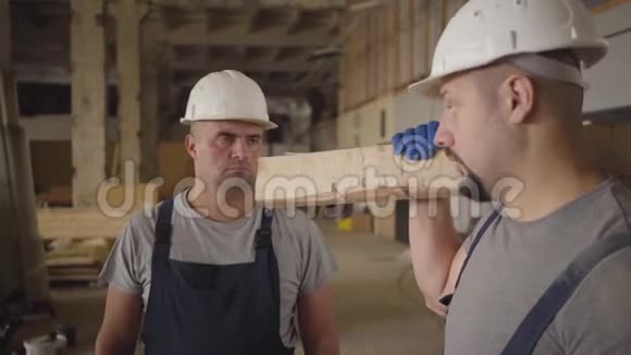 两名戴着白盔的白种人成年建筑工人在施工现场交谈一个工人带着视频的预览图