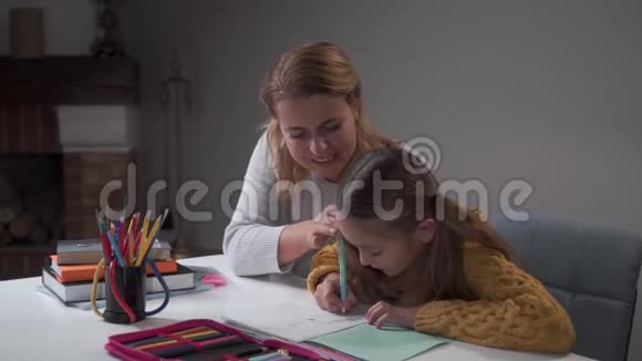 年轻的白种人女家教在家教可爱的小女孩作业本中聪明的学童书写老师视频的预览图