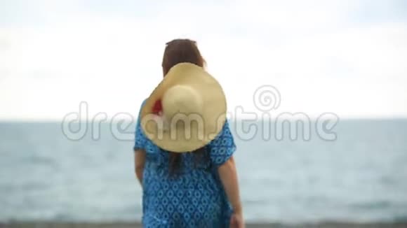生活方式漂亮的女人带着一顶大帽子在海滩上散步视频的预览图