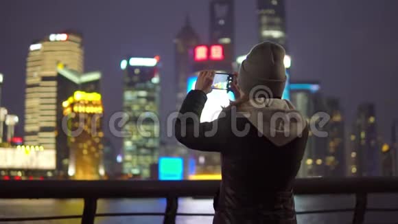 一个穿着黑色夹克和帽子的年轻女孩用手机拍下了上海景点的照片视频的预览图