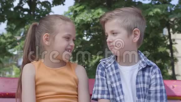 可爱的男孩和可爱的女孩坐在公园里的秋千上聊天跳舞玩得很开心一对快乐视频的预览图