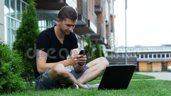 男生坐在草地上使用手机和笔记本电脑视频的预览图