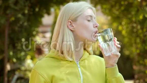 美女从绿色公园的玻璃上喝水清洁卫生水视频的预览图