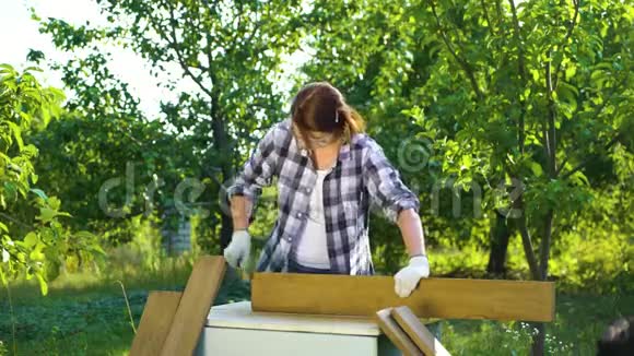 在阳光明媚的花园里工匠妇女用金属刷子手工打磨旧木板视频的预览图