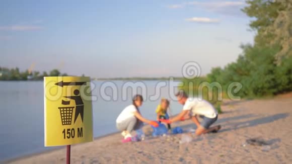 垃圾桶上的指针标志带着小孩的年轻家庭在肮脏的沙滩上用塑料收集垃圾视频的预览图