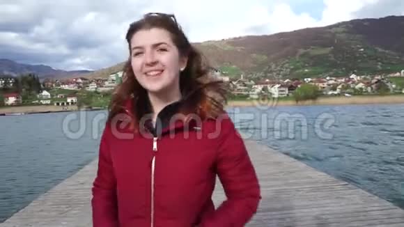 女人独自走在木墩上穿着红色夹克在黑山山区的一个湖里度假的快乐女孩视频的预览图