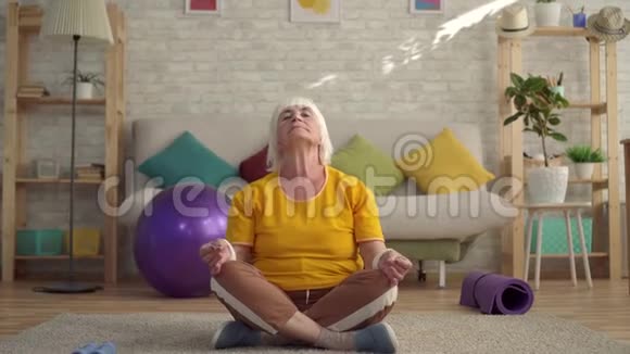 积极向上的老妇人在客厅的地毯上做瑜伽视频的预览图