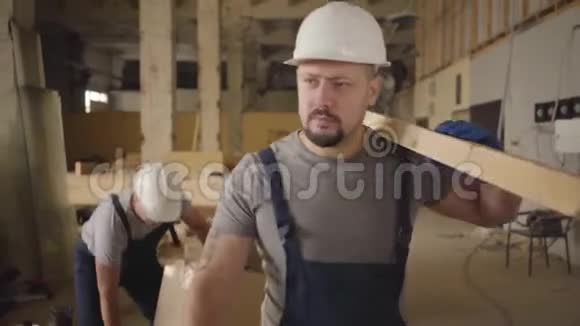成年白种人戴着白色头盔穿着蓝色制服用木板在施工现场行走建设者视频的预览图