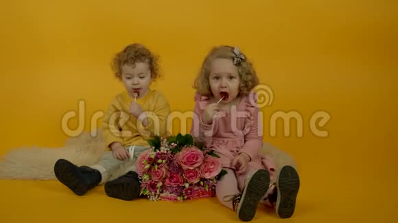 两个带着鲜花的孩子在地毯上吃棒棒糖视频的预览图
