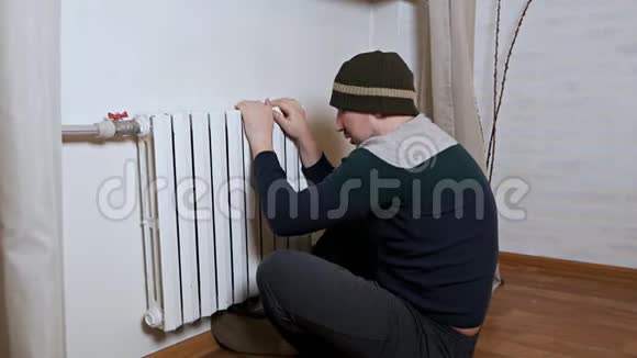 一个戴帽子的人把手放在靠近墙壁的暖气片上取暖公寓里冷供暖系统差视频的预览图