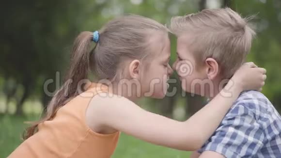 侧面看可爱的男孩和女孩坐在公园里摩擦鼻子玩得开心一对幸福的孩子视频的预览图