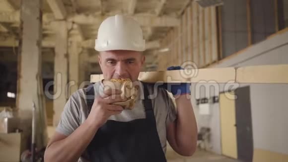 一个肌肉发达的高加索建筑工人的肖像棕色的眼睛在建筑工地吃面包强壮的年轻工人视频的预览图