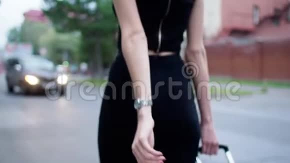 穿着黑色连衣裙带手提箱的女孩走在城市街道上度假视频的预览图