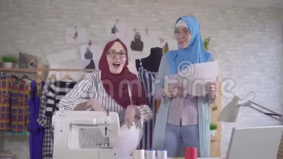 两位积极的穆斯林女青年时装设计师在国家头巾扔文件高兴视频的预览图