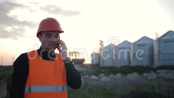 戴着头盔的工程师在智能手机上谈论工厂的背景创造新技术视频的预览图