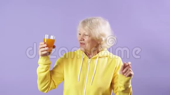 一位身穿黄色运动衫手里拿着一杯新鲜胡萝卜汁的快乐老妇人视频的预览图