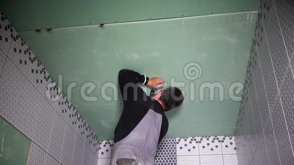 累了的工人用螺丝刀把石膏板石膏板固定在天花板上视频的预览图