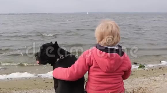 秋天的下午女孩和她的黑狗坐在河岸上看着水视频的预览图