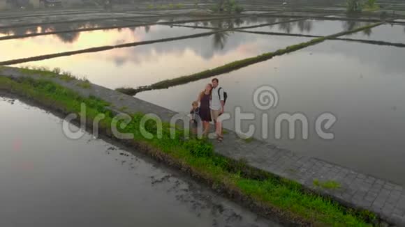 一个幸福的家庭站在人行道上穿过被水填满的大田野他们喜欢日落视频的预览图