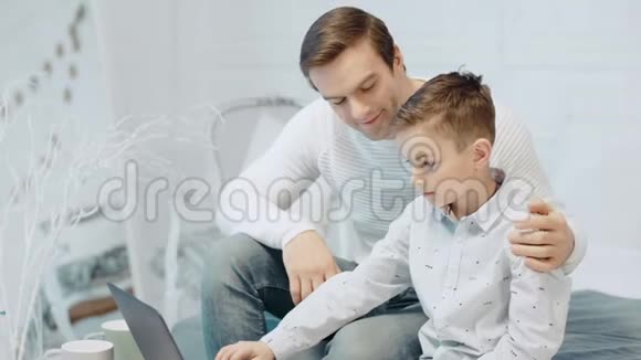 阿皮爸爸抱着儿子在现代公寓里看电脑屏幕视频的预览图