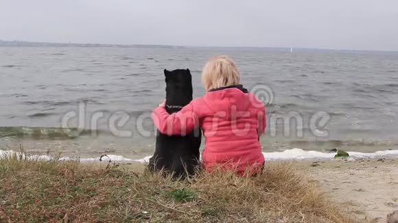 秋天的下午女孩和她的黑狗坐在河岸上看着水视频的预览图