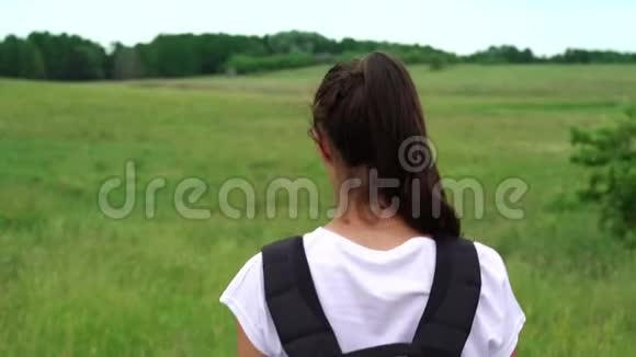年轻的美女背着黑色背包沿着草地散步视频的预览图