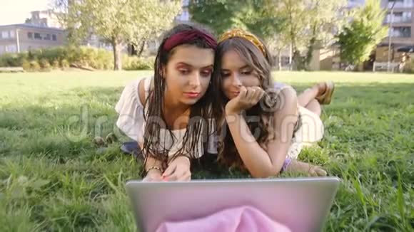 两个女朋友姐妹躺在草地上在公园里看电影两个黑发女人躺在公园的草地上放松视频的预览图