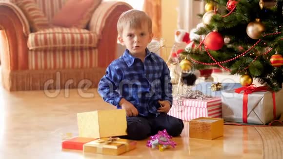 4k视频愤怒的男孩坐在圣诞树下大喊因为他点了不需要的礼物和礼物视频的预览图