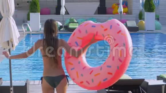 一个苗条的女孩穿着游泳衣头发湿漉漉的戴着充气戒指在暑假度假胜地跑步跳进游泳池视频的预览图