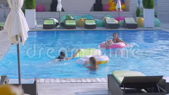 一群快乐的女朋友在游泳池里放松女朋友带着充气环跳到水旁边视频的预览图