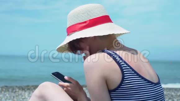 近景海边抽象背景下手持智能手机的年轻女子视频的预览图