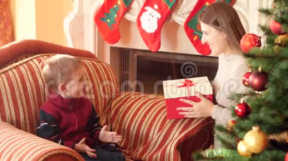 4k视频小母亲送给坐在漂亮圣诞树旁的小儿子圣诞礼物视频的预览图