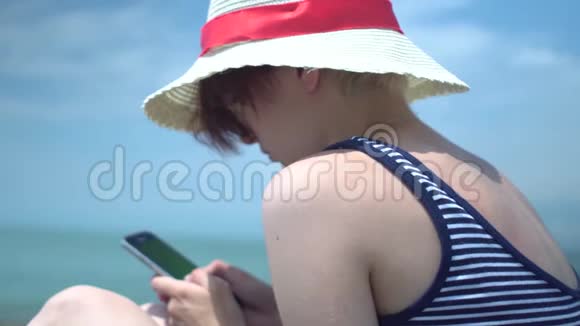 年轻的美女使用智能手机戴着复古帽子穿着蓝色和白色泳衣的信使应用程序输入文字视频的预览图