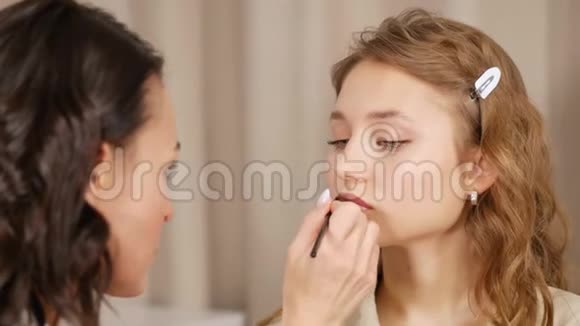 化妆师在客户脸上化妆在女孩的嘴唇上涂上油漆视频的预览图