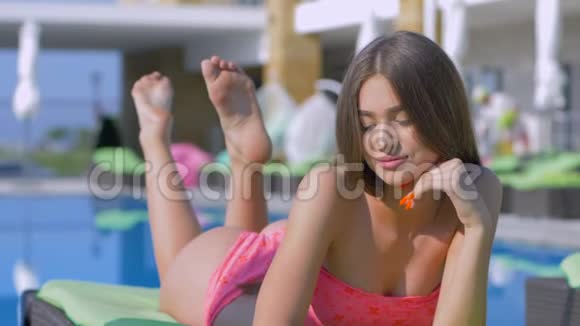 夏季放松迷人的女孩穿上泳衣休息和日光浴在游泳池边的甲板椅上度假视频的预览图