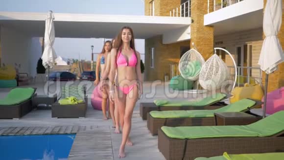 度假村里的女孩们穿着泳装的漂亮长发女朋友在游泳池边漫步在夏天的休息室里快乐地陪伴着她们视频的预览图