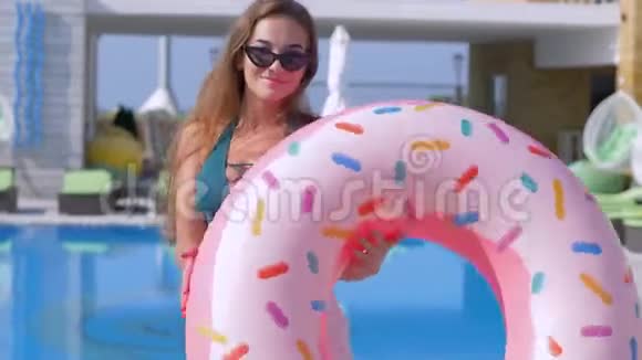 漂亮迷人的女孩穿着泳衣和带充气戒指的眼镜在昂贵的游泳池附近的相机上调情视频的预览图