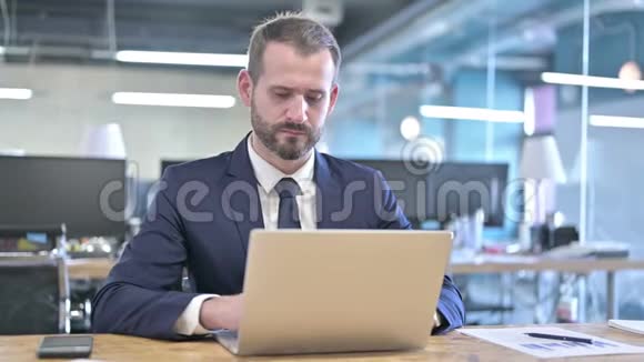 在办公桌上操作笔记本电脑的雄心勃勃的商人视频的预览图