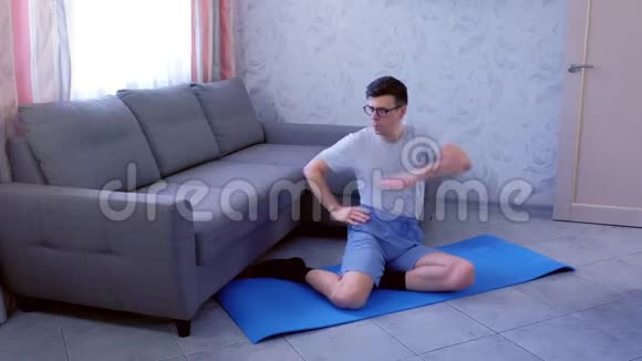 有趣的书呆子男子正在做躯干扭转运动坐在垫子在家里体育幽默概念视频的预览图